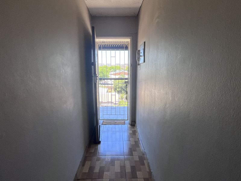 A narrow hallway featuring tiled flooring, an intercom system, and a security gate leading to an outdoor area.