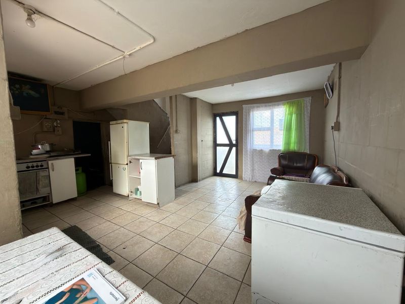 Open-plan living and kitchen area featuring tiled flooring and exposed structural elements, offering a functional space with potential for modernization and renovation.