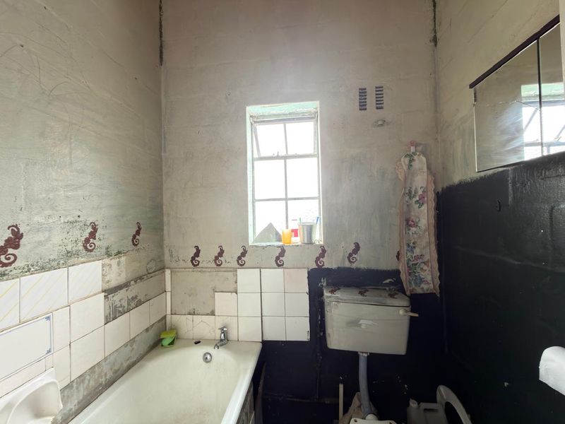 A bathroom in need of significant renovation, featuring a bathtub, toilet cistern, and window, with unfinished wall surfaces and missing tile work.
