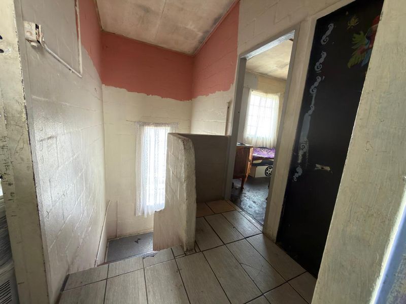 A hallway area featuring tiled flooring and masonry walls, currently in need of cosmetic updates and finishing to improve its overall condition.