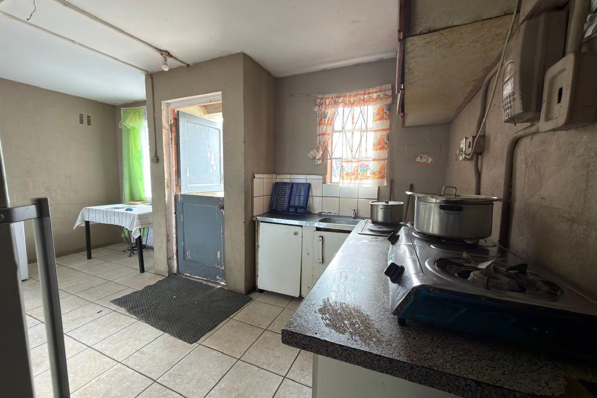 A dated kitchen featuring tiled flooring, basic cabinetry, and a stainless steel sink, requiring significant renovation and cosmetic updates to improve functionality and aesthetic appeal.