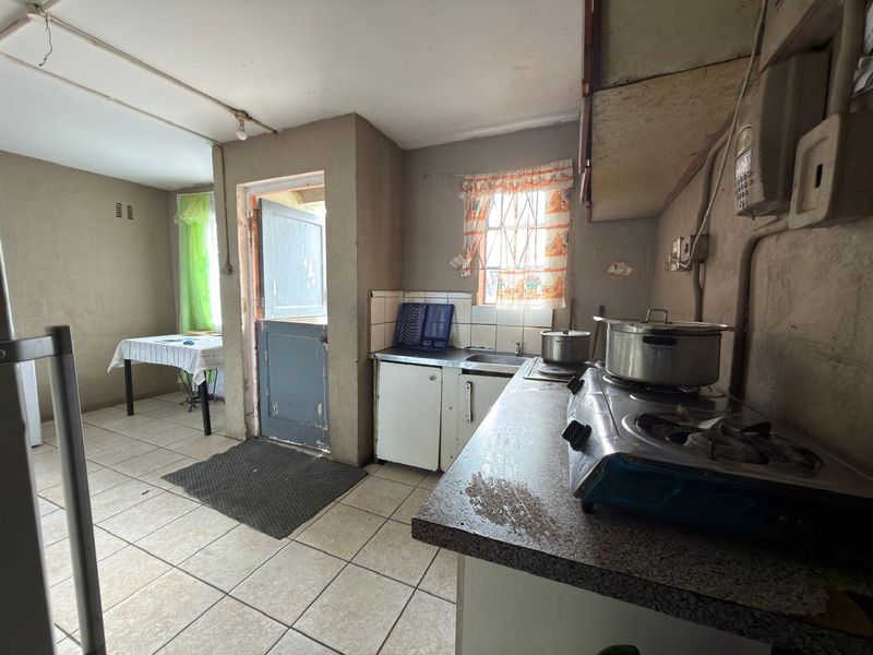 A dated kitchen featuring tiled flooring, basic cabinetry, and a stainless steel sink, requiring significant renovation and cosmetic updates to improve functionality and aesthetic appeal.