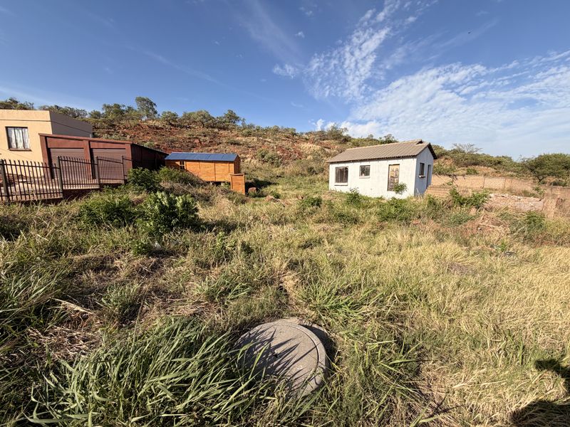 A view of the rear yard featuring an overgrown landscape, a small detached outbuilding, a wooden shed, and a concrete inspection cover.