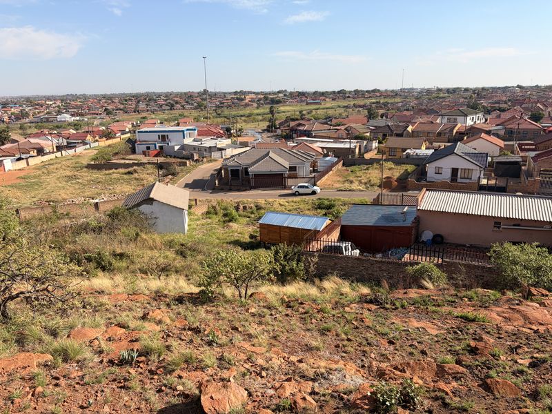 An elevated aerial view overlooking a residential neighborhood with surrounding undeveloped rocky land and local housing infrastructure.