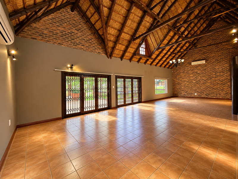 Spacious living area featuring high vaulted ceilings with exposed timber trusses, exposed brick walls, ceramic tile flooring, and large sliding doors leading outdoors.