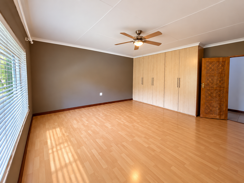 Spacious bedroom featuring light wood-look laminate flooring, extensive built-in cabinetry, a ceiling fan, and venetian blinds on the window.