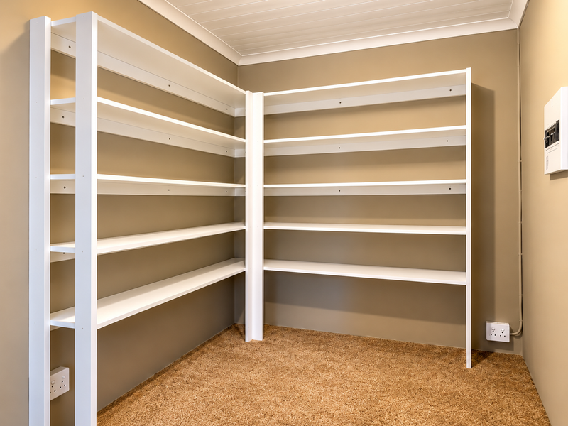 A clean, empty utility or storage space featuring extensive built-in white shelving, neutral wall finishes, and practical electrical infrastructure.