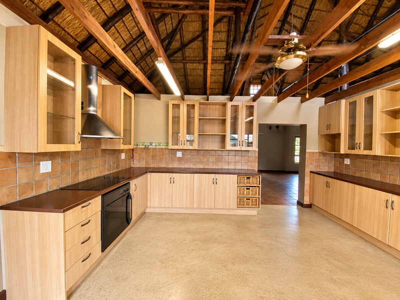 Spacious kitchen featuring light wood cabinetry, dark laminate countertops, tiled backsplash, and a unique high-volume thatched ceiling with exposed timber rafters.