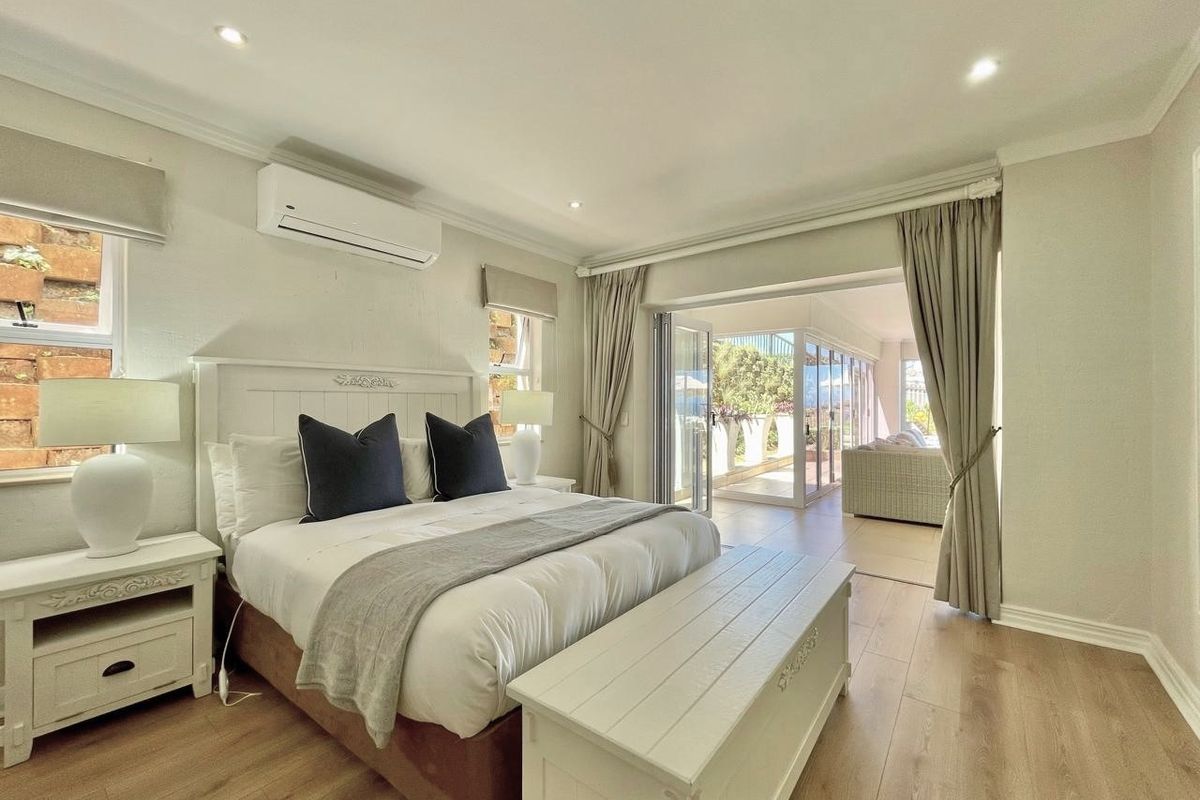 Spacious bedroom featuring laminate flooring, recessed lighting, and a split-system air conditioner, with direct access to an adjoining patio through bi-fold doors.
