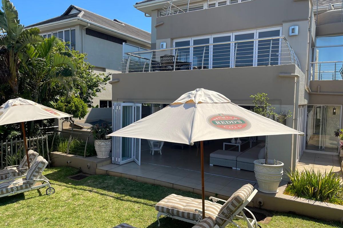 Rear view of the apartment featuring a landscaped garden, tiled patio area with bi-fold doors, and an upper-level balcony with stainless steel balustrades.