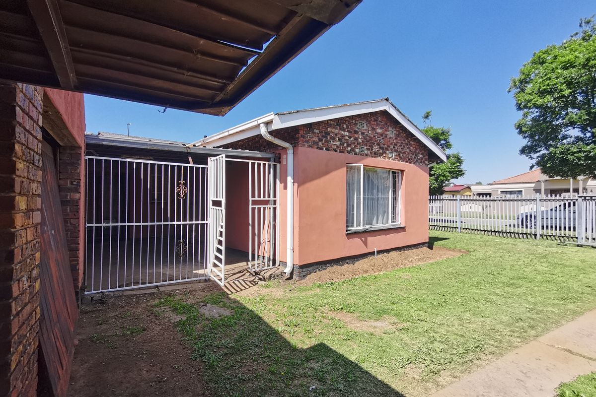 Rear view of the property featuring a brick and rendered facade, metal security gate, and a small lawn area.