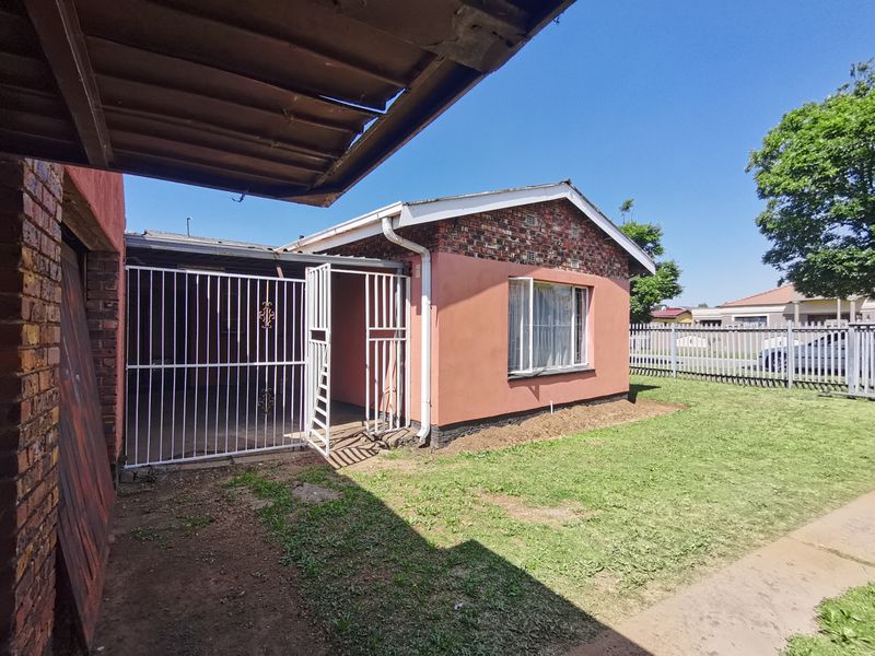 Rear view of the property featuring a brick and rendered facade, metal security gate, and a small lawn area.