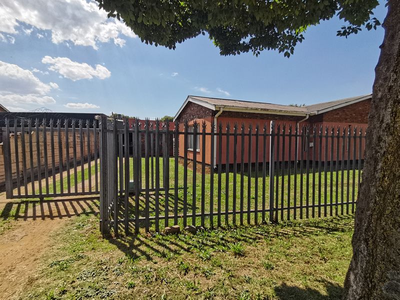 Front view of the property featuring a brick facade, pitched roof, and secure steel palisade fencing with a sliding gate.
