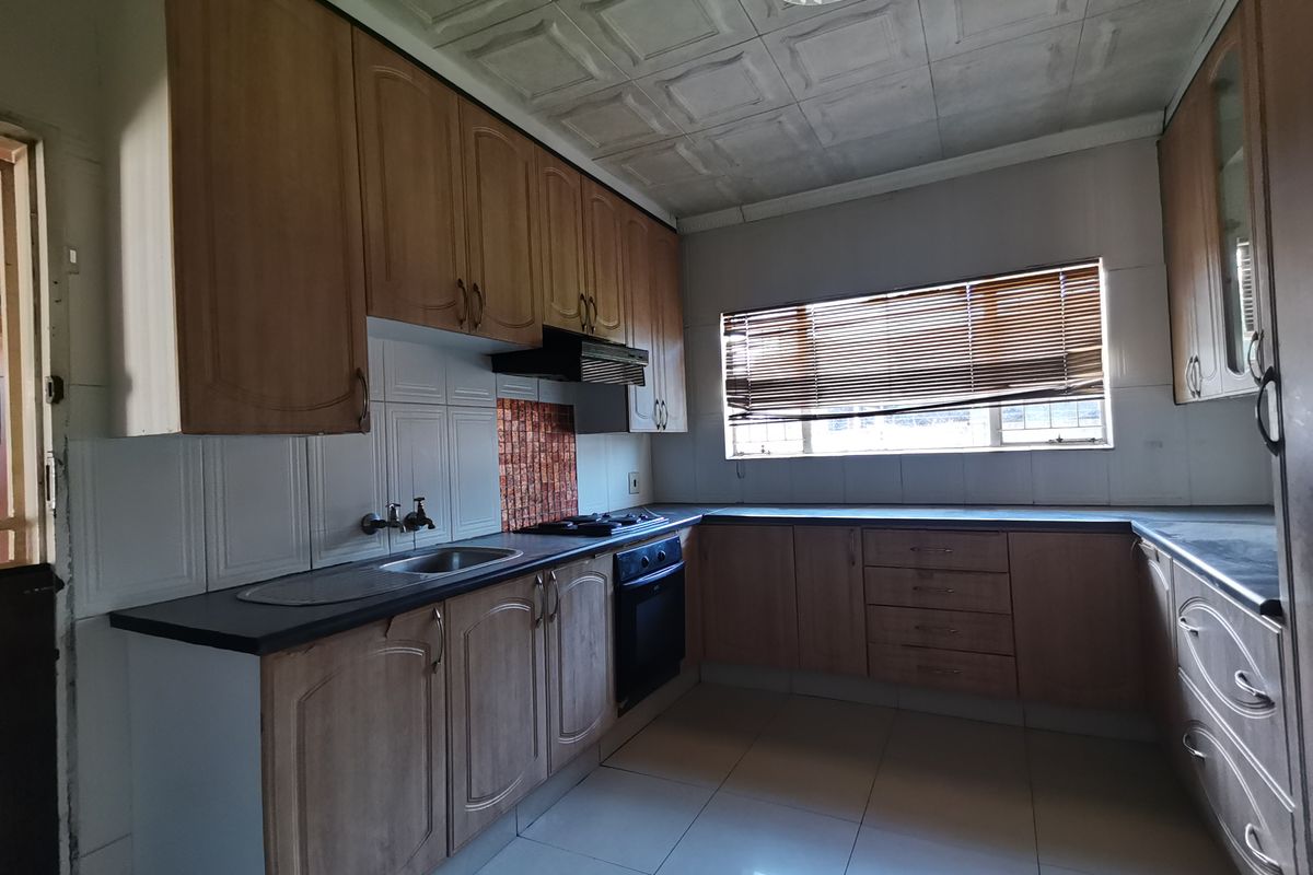 A functional kitchen featuring built-in wooden cabinetry, laminate countertops, integrated oven and hob, and tiled flooring, offering a practical layout for culinary activities.