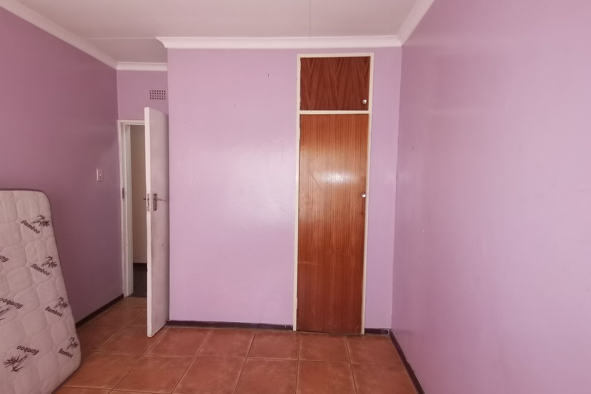 A vacant bedroom featuring tiled flooring, purple painted walls, and a built-in wooden cupboard.