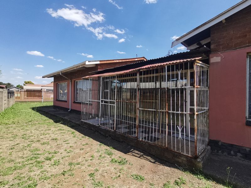 Rear view of the property featuring a covered patio area with security bars, brick exterior walls, and a surrounding garden space.
