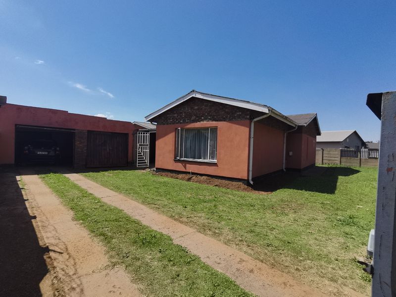 Front view of a single-story house featuring a attached garage, driveway, and brick and rendered facade.