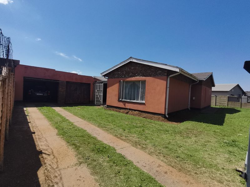 Front exterior view of a single-story house featuring a brick driveway, attached garage, and security fencing.