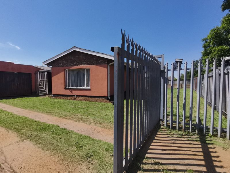 Front view of a single-story house featuring a brick facade, tiled roof, and secure metal perimeter fencing with a gated entrance.