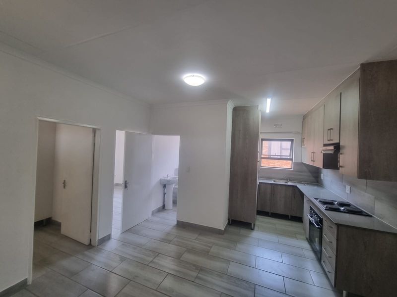 An open-plan kitchen and living area featuring modern wood-look cabinetry, built-in appliances, and neutral tiled flooring, with direct access to adjacent rooms.