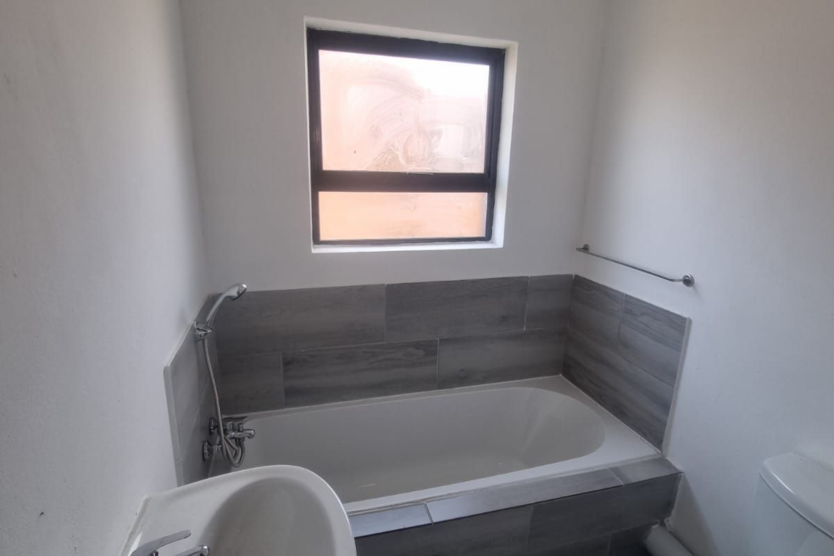 A clean, functional bathroom featuring a bathtub with tiled surround, pedestal basin, and toilet, finished with modern grey floor and wall tiles.