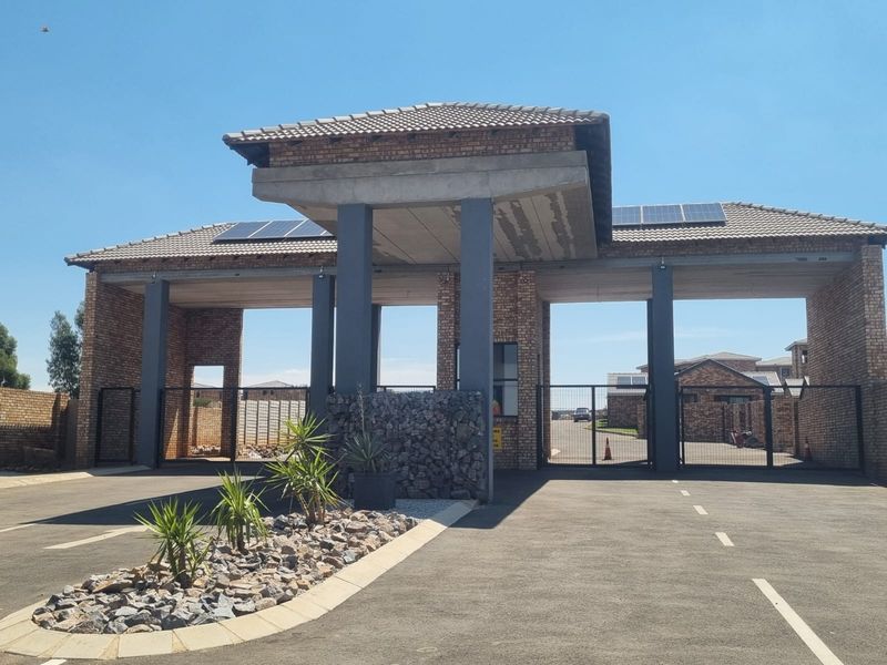 The main entrance gatehouse of the apartment complex features a brick facade, solar panels, and secure gated access.