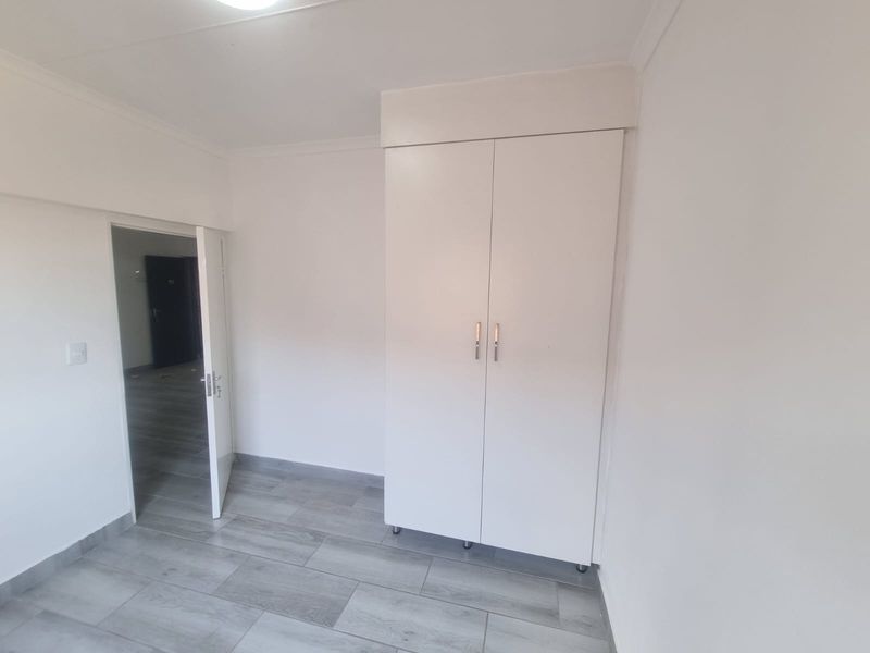 A clean, empty bedroom featuring modern grey wood-look floor tiles and a white built-in wardrobe.