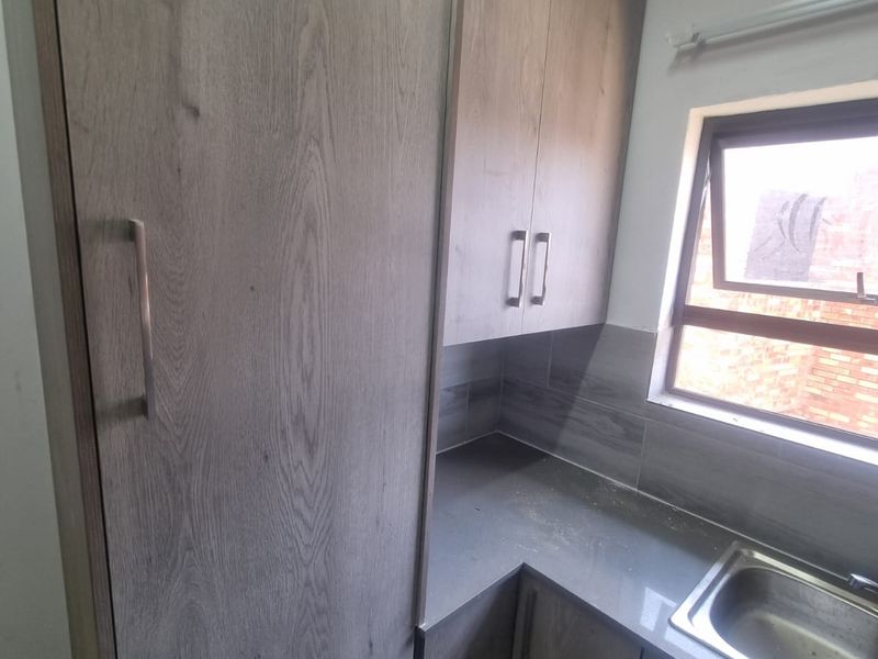 A compact scullery area featuring modern wood-grain cabinetry, stone countertops, a stainless steel sink, and a tiled backsplash.