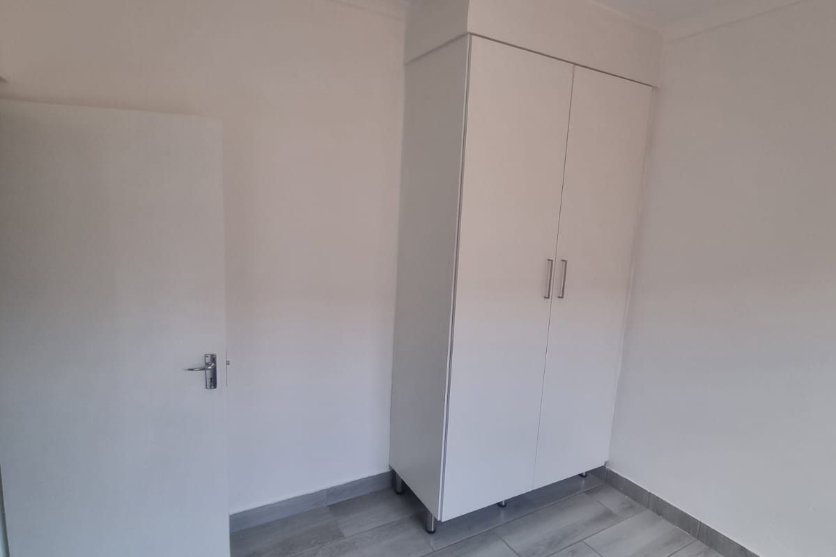 A clean, empty bedroom featuring modern grey wood-look floor tiles and a white built-in wardrobe.
