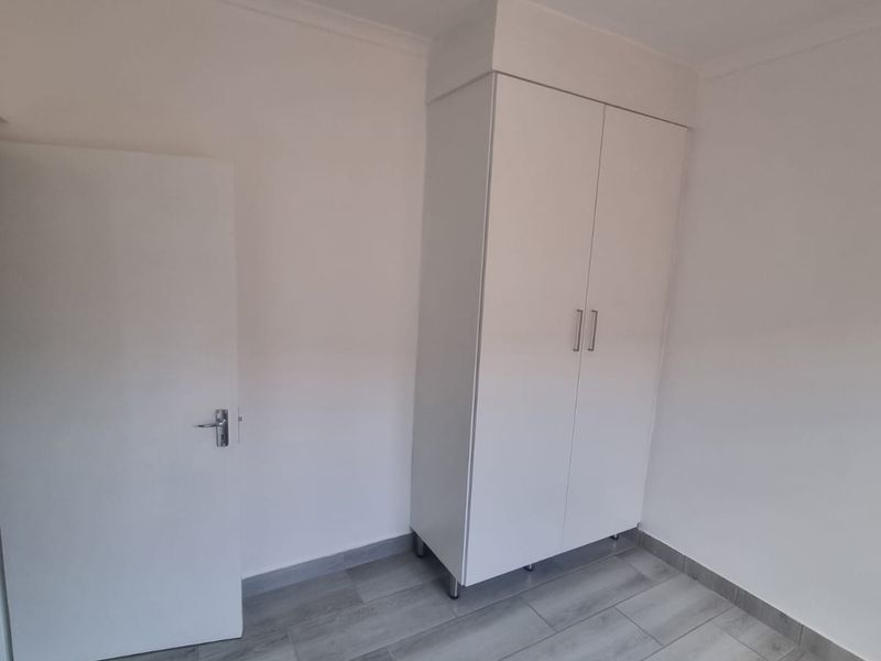 A clean, empty bedroom featuring modern grey wood-look floor tiles and a white built-in wardrobe.