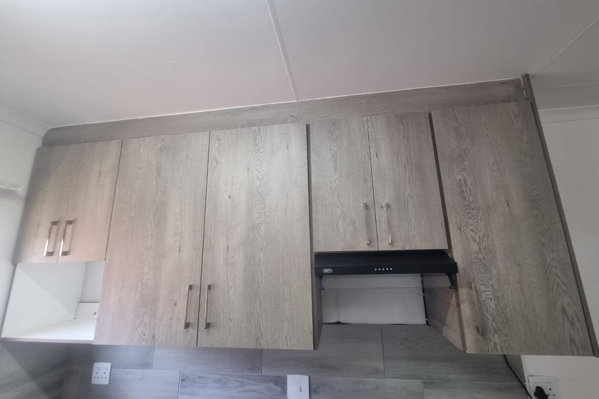 A modern kitchen featuring light wood-grain cabinetry, a built-in extractor fan, and a contemporary tiled backsplash with integrated electrical outlets.
