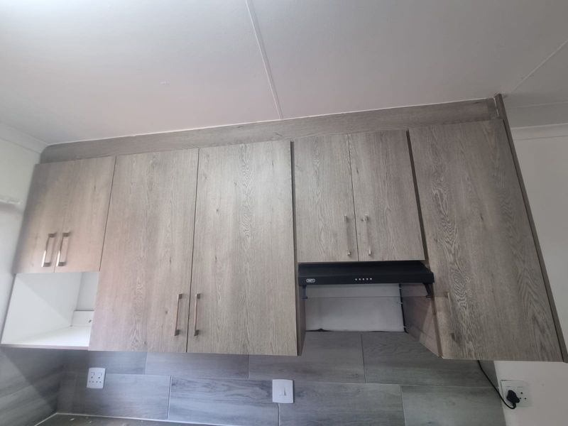 A modern kitchen featuring light wood-grain cabinetry, a built-in extractor fan, and a contemporary tiled backsplash with integrated electrical outlets.