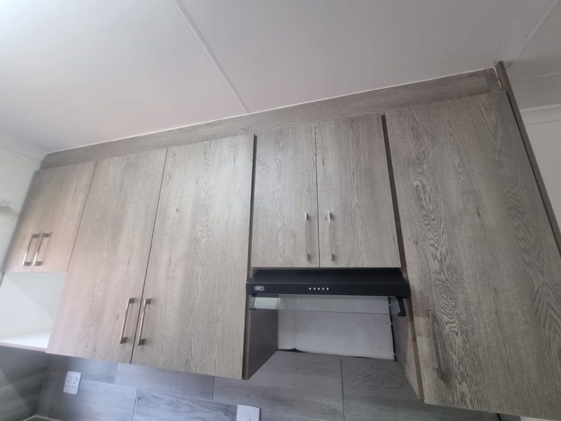 A modern kitchen featuring light wood-grain cabinetry, a built-in extractor fan, and a contemporary tiled backsplash.