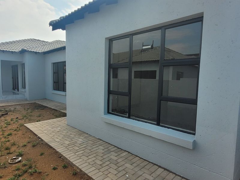 Rear view of the property featuring a paved walkway, aluminium window frames, and an unfinished garden area.