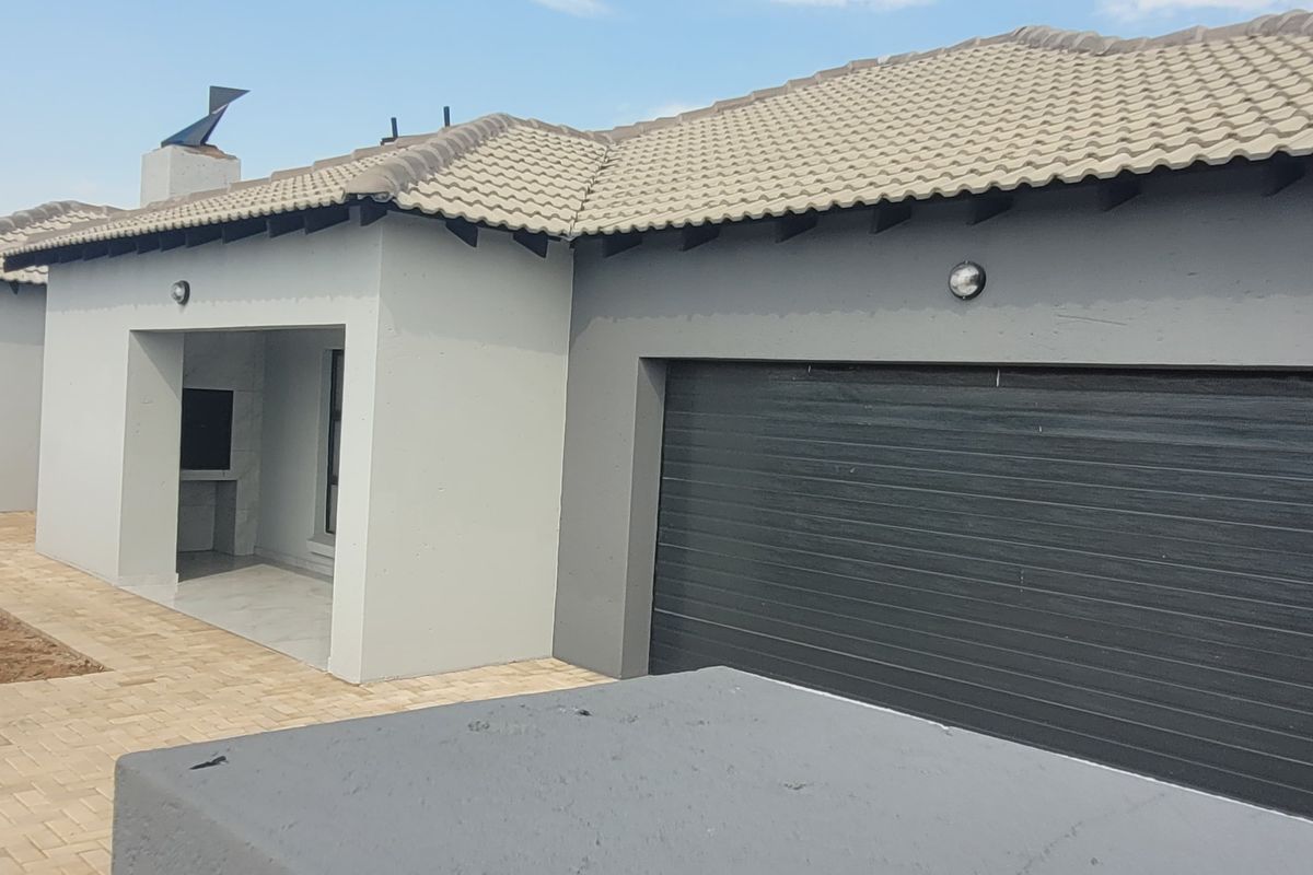 Rear view of the house featuring a paved patio area with a built-in braai and an integrated garage.