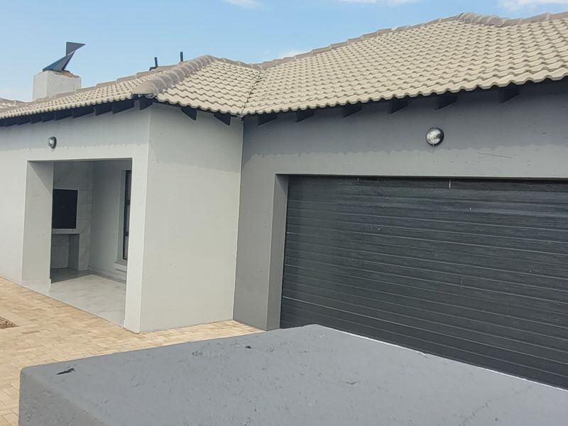 Rear view of the house featuring a paved patio area with a built-in braai and an integrated garage.