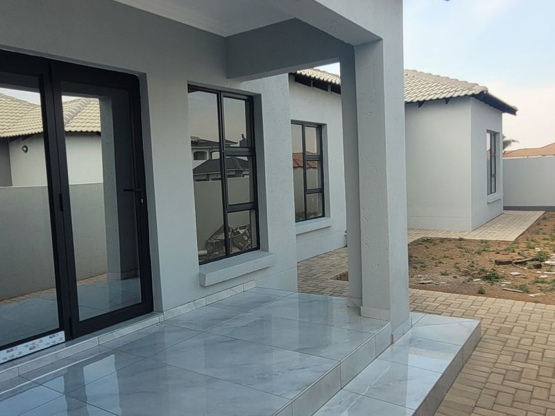 A modern covered patio featuring large format tiles and black aluminium sliding doors, leading out to an unfinished garden area with paved pathways.