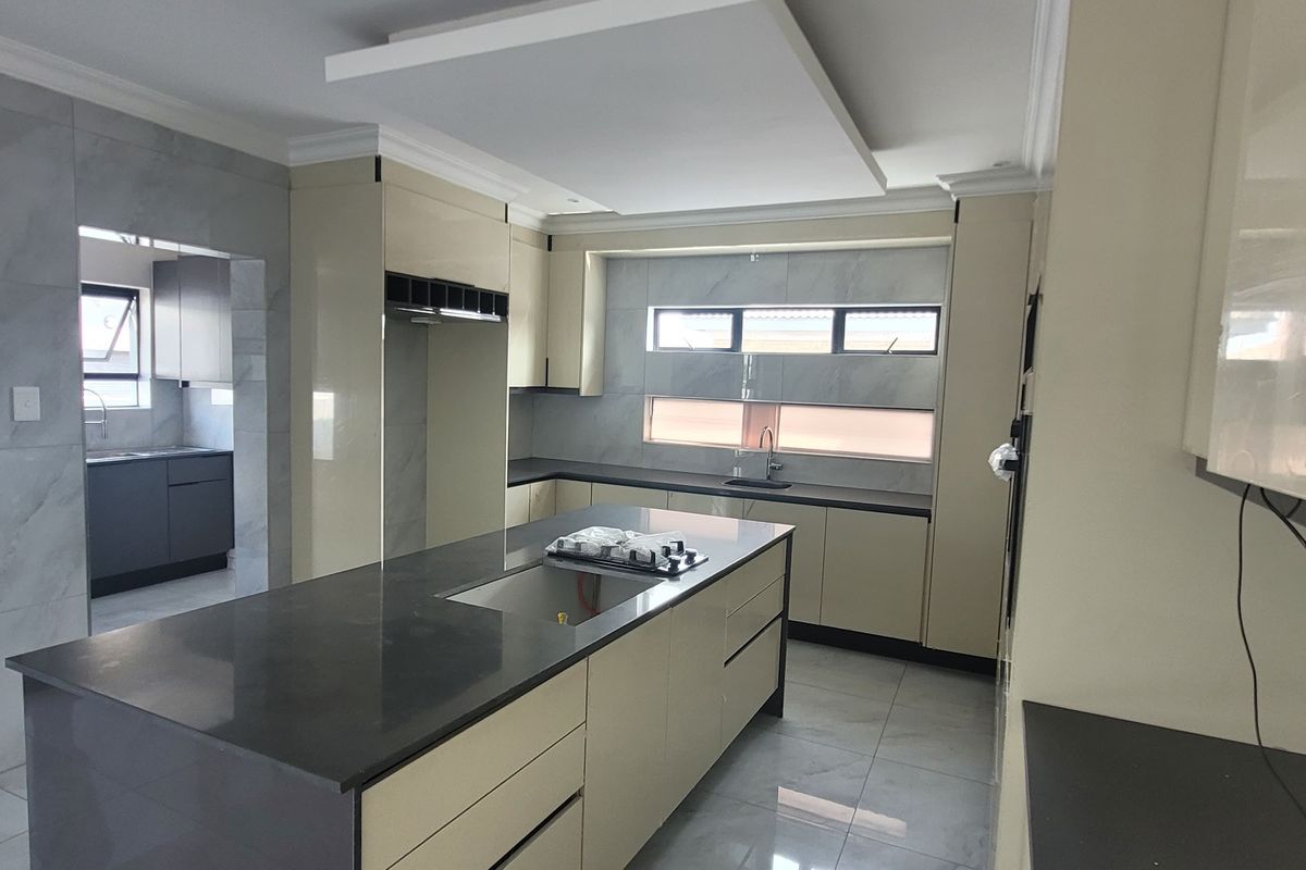 Modern kitchen featuring a large central island with stone countertops, sleek built-in cabinetry, tiled finishes, and a contemporary drop ceiling design.