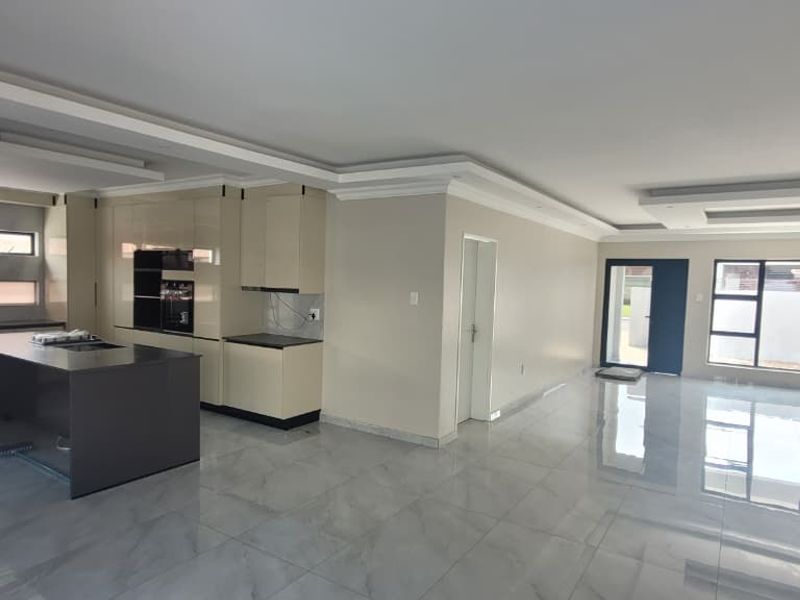 Spacious open-plan living and kitchen area featuring modern high-gloss cabinetry, a central island, tiled floors, and recessed ceiling lighting in a contemporary home.