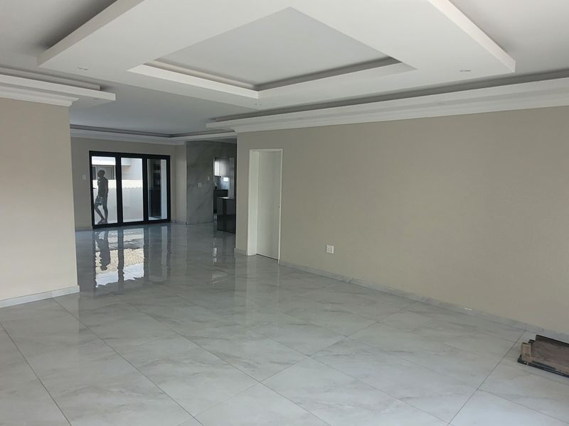 Spacious open-plan living area featuring modern recessed ceiling details, neutral wall finishes, and large-format porcelain floor tiles throughout.