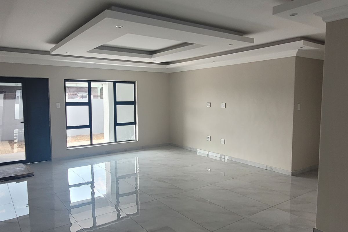 A spacious, modern living area featuring high-gloss porcelain tiles, a sophisticated recessed ceiling with downlights, and large aluminium-framed windows.