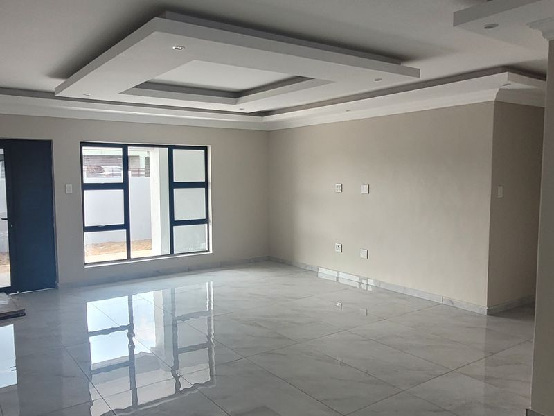 A spacious, modern living area featuring high-gloss porcelain tiles, a sophisticated recessed ceiling with downlights, and large aluminium-framed windows.