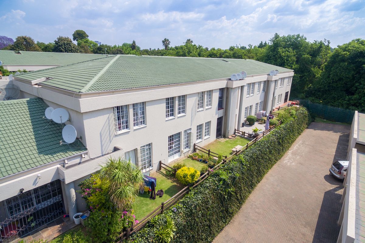 Aerial view of a multi-unit apartment complex featuring tiled roofing, private garden spaces with fencing, and a paved driveway area.