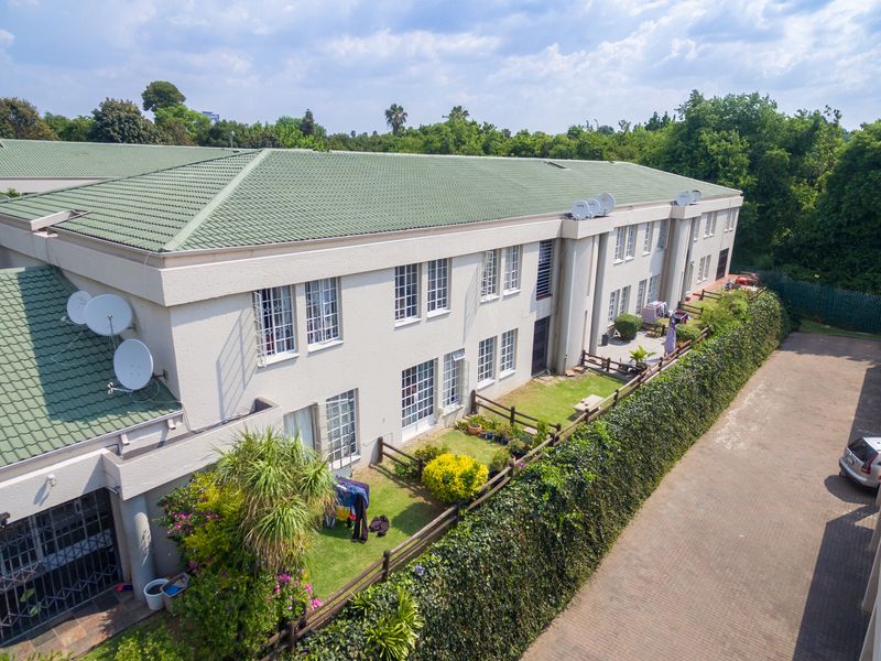 Aerial view of a multi-unit apartment complex featuring tiled roofing, private garden spaces with fencing, and a paved driveway area.