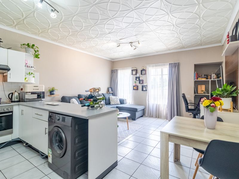 Open-plan living area featuring a functional kitchen with built-in appliances, tiled flooring, and unique decorative ceiling tiles, creating a versatile and connected living space.