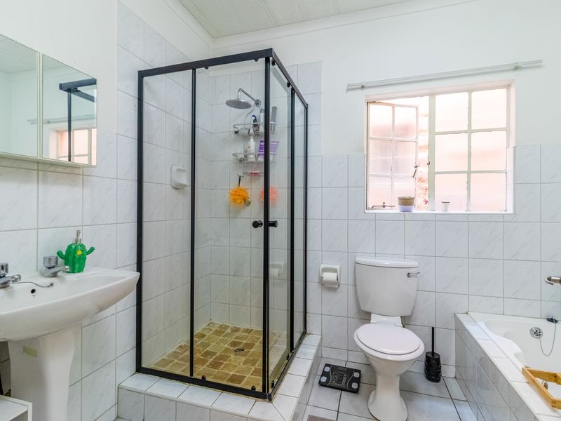A functional bathroom featuring a pedestal basin, a separate shower enclosure with black frame, a toilet, and a bathtub with tiled finishes throughout.