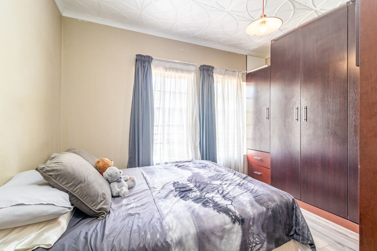 A bedroom featuring a built-in dark wood wardrobe, textured ceiling, and laminate flooring, offering a functional space with natural light.