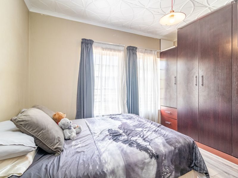 A bedroom featuring a built-in dark wood wardrobe, textured ceiling, and laminate flooring, offering a functional space with natural light.