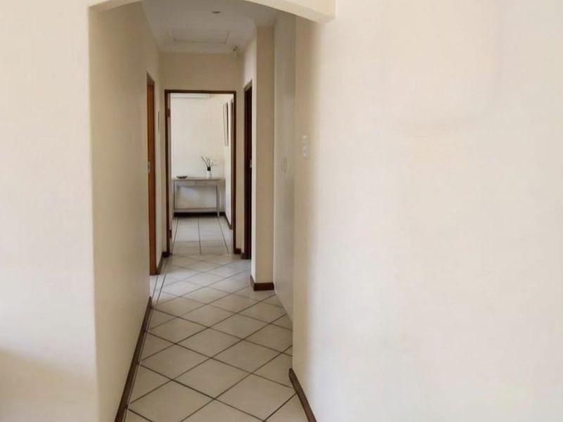A clean, neutral hallway featuring tiled flooring and an arched entryway leading to adjacent rooms.