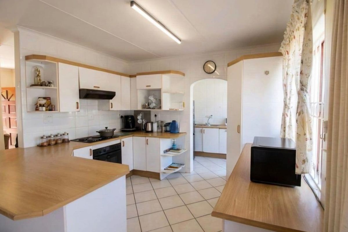 A functional kitchen featuring white cabinetry, wood-look laminate countertops, tiled flooring, and an adjoining scullery area through an arched doorway.